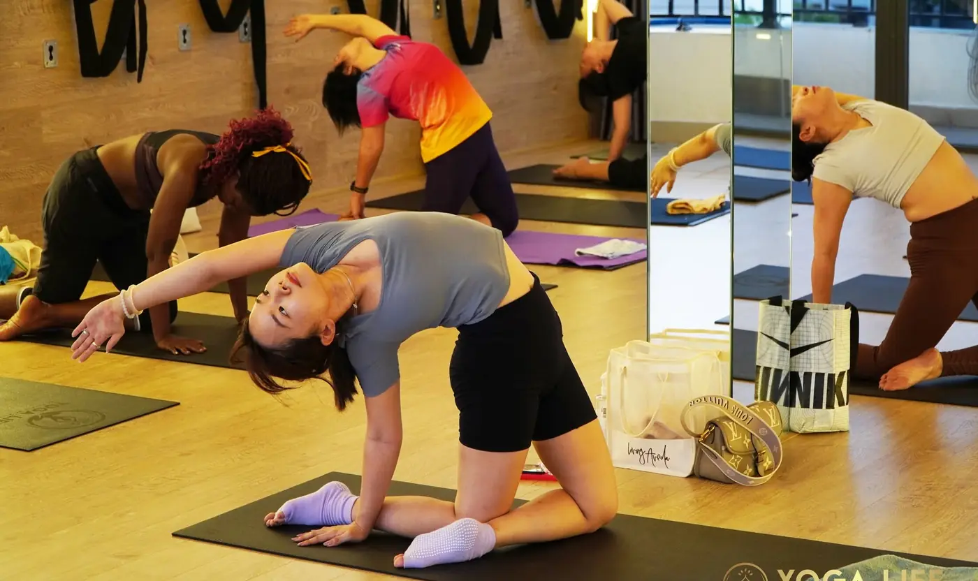 A group class practising a kneeling backbend beside the wall ropes in the studio