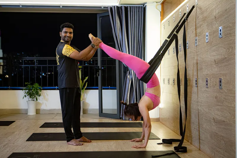A teacher spotting a student in a supported handstand at the wall