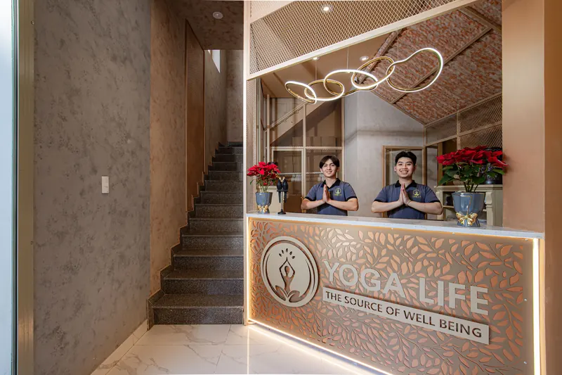 The reception desk at Yoga Life Premium, with two of the team welcoming visitors beneath the gold ring lights